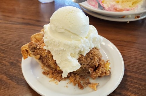 A slice of apple pie topped with a generous scoop of vanilla ice cream on a white plate.