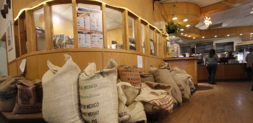 A cozy café interior with burlap sacks stacked in front of a wooden counter and a menu board on the wall.