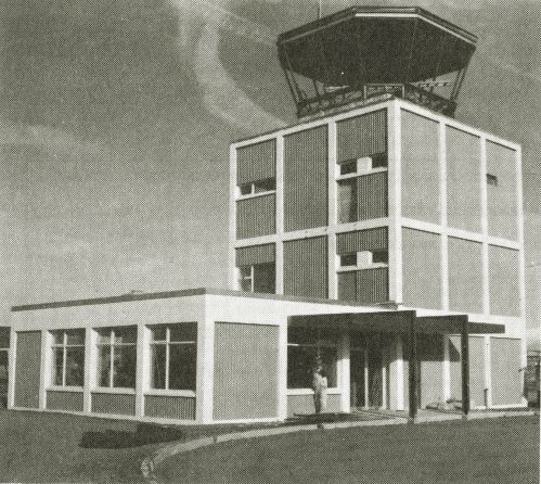 Black and white image of a modern airport control tower with a flat-roofed building at its base.