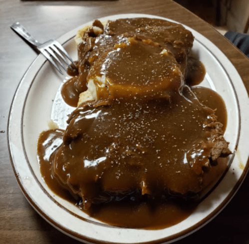 A plate of meatloaf covered in brown gravy, served with mashed potatoes, on a wooden table.