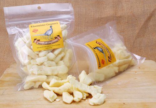 Two bags of Käsemeister Creamery Mild Cheddar Cheese curds on a wooden surface, with one bag partially open.
