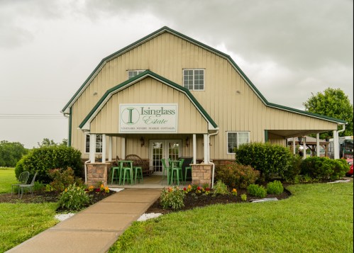 A charming vineyard cottage with a green roof and sign, surrounded by well-kept gardens and a pathway.