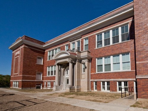 Historic brick building with large windows and a decorative entrance, set against a clear blue sky.