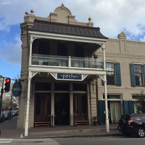 A historic building with a balcony, featuring the sign "pêche" and large wooden doors, under a partly cloudy sky.