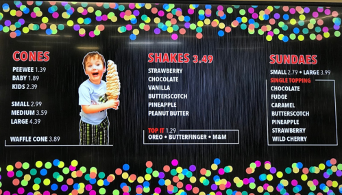 A child holding a large ice cream cone, with a colorful menu of cones, shakes, and sundaes in the background.