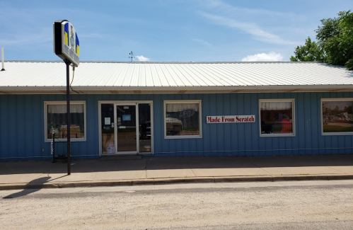 A blue building with a metal roof, featuring a sign that says "Made From Scratch" and an "Open" sign in the window.