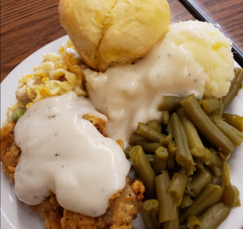 A plate of comfort food featuring fried chicken with gravy, mashed potatoes, green beans, macaroni, and a biscuit.