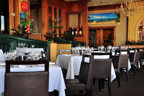 Elegant restaurant interior with tables set for dining, featuring green booths, plants, and a scenic mural.