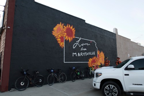 Mural reading "Love from Marysville" with sunflowers, bikes parked nearby, and people in the background.