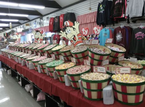 A colorful display of candy in large baskets, with a festive shop interior and merchandise in the background.