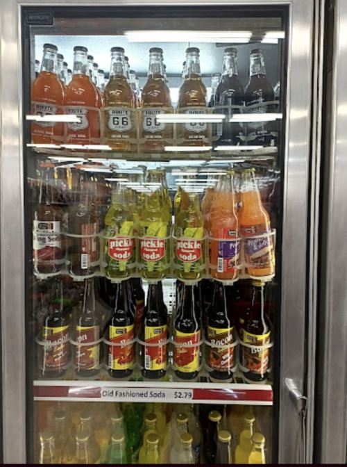 A refrigerator filled with various colorful soda bottles, including unique flavors like pickle and bacon soda.