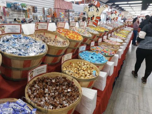 A colorful display of various candies in baskets at a candy store, with shoppers browsing the selection.