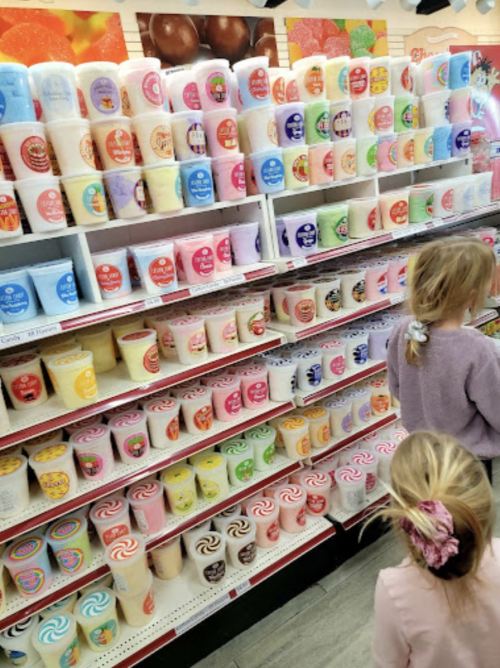 Two children look at a colorful display of ice cream tubs on shelves in a store.