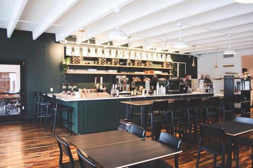 A modern café interior featuring a dark green counter, wooden floors, and stylish seating.