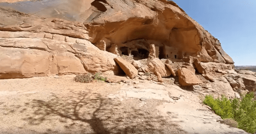 Ancient stone structures nestled in a rocky cliff, surrounded by desert landscape and clear blue sky.