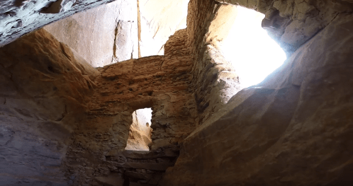 Interior of a rocky cave with natural light streaming through openings, highlighting textured stone walls.