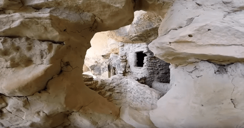 View through a rock formation revealing ancient stone structures and caves in a rugged landscape.
