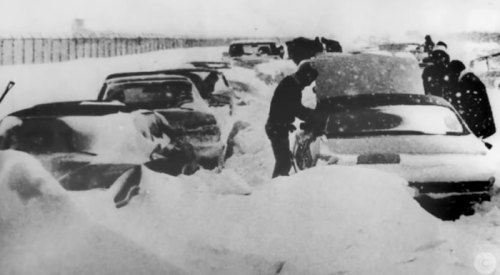 A snowy scene with cars buried in snow, people digging out vehicles during a severe winter storm.