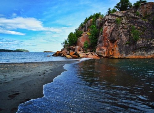 A serene beach scene with rocky cliffs, calm water, and a clear blue sky.