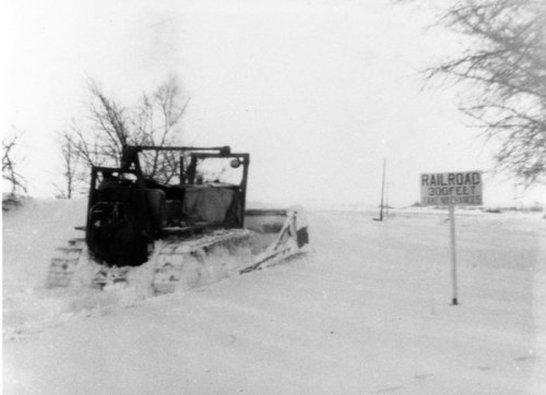 A snowplow clears a snowy railroad track, with a sign indicating the railroad is 300 feet ahead.