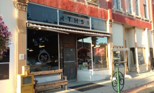 A storefront with "NORTHSIDE" signage, featuring large windows and a wooden bench outside, in a vibrant urban setting.