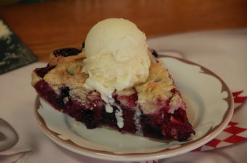 A slice of berry pie topped with a scoop of vanilla ice cream on a decorative plate.