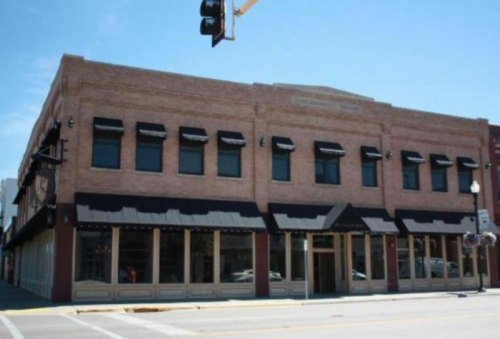A brick building with large windows and awnings, located at a street corner under a clear blue sky.