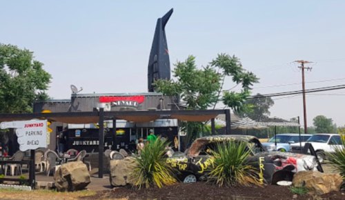 A quirky restaurant with a large rocket sculpture on the roof, surrounded by outdoor seating and greenery.