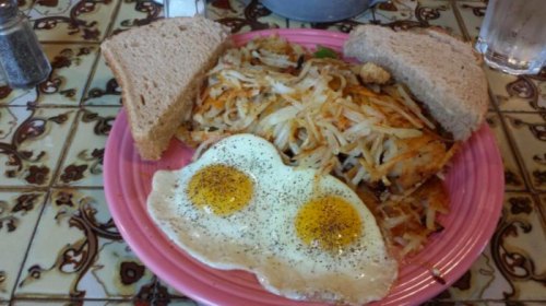 A plate of breakfast featuring two fried eggs, hash browns, and two slices of whole grain bread.