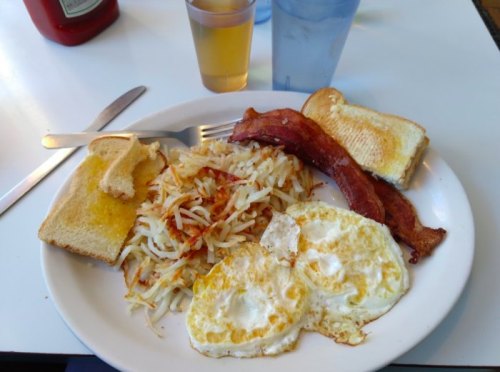 A plate of breakfast featuring eggs, bacon, hash browns, toast, and drinks on a table.