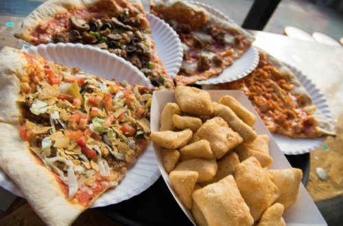 A variety of pizza slices on paper plates, including toppings like vegetables and cheese, alongside a serving of breadsticks.