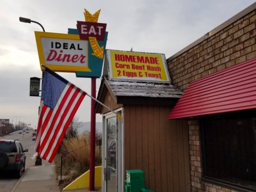 Sign for Ideal Diner featuring "Homemade Corn Beef Hash, 2 Eggs & Toast" with an American flag in front.