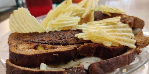 A sandwich on a plate topped with potato chips, featuring dark bread and visible layers of filling.
