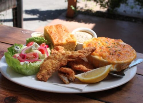 A plate of fried fish, cornbread, salad, and a creamy dish, garnished with a lemon wedge.