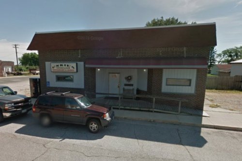 A brick building with a sign reading "Junkie" and a porch, set on a quiet street with parked cars nearby.