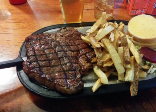A grilled steak with crosshatch marks, served with golden fries and a slice of bread on a metal platter.