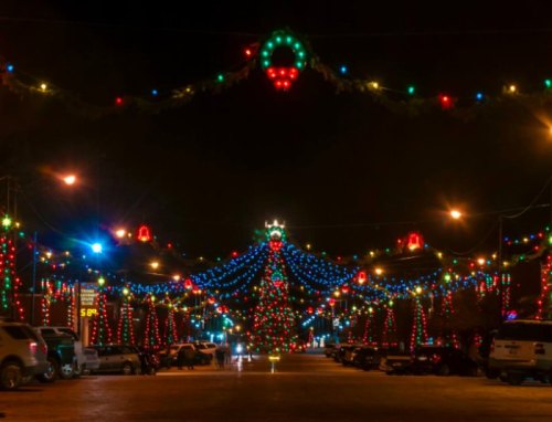 A festive street adorned with colorful Christmas lights and decorations, creating a cheerful holiday atmosphere at night.