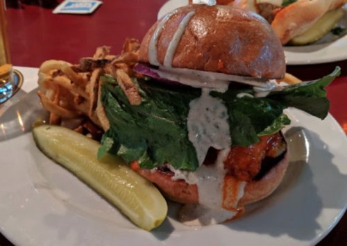 A hearty burger topped with lettuce, sauce, and pickles, served with crispy fries on a plate.