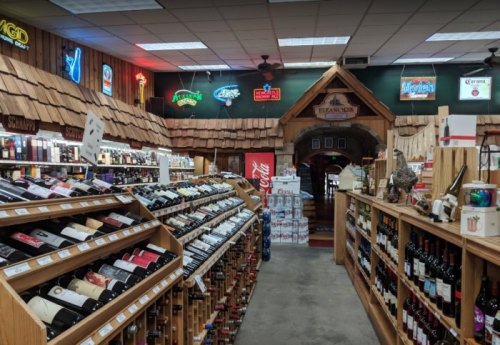 Interior of a wine shop with wooden shelves filled with bottles, neon signs, and a cozy, rustic atmosphere.