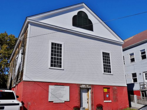 Historic building with a white upper facade, large windows, and a red lower section against a clear blue sky.