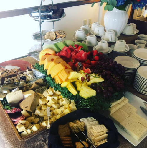 A colorful spread of fruits, cheeses, and snacks on a table, with plates and cups in the background.