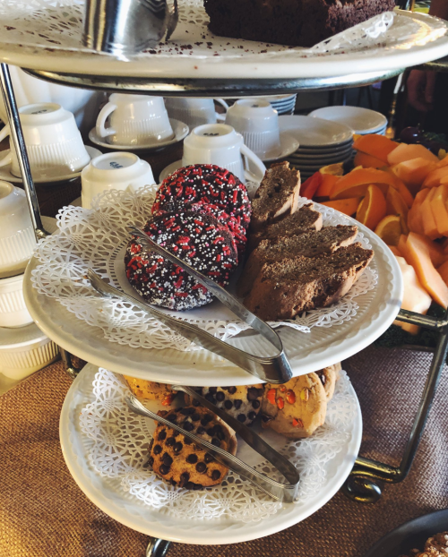 A tiered dessert stand with assorted cookies, brownies, and fruit, set against a rustic tablecloth.