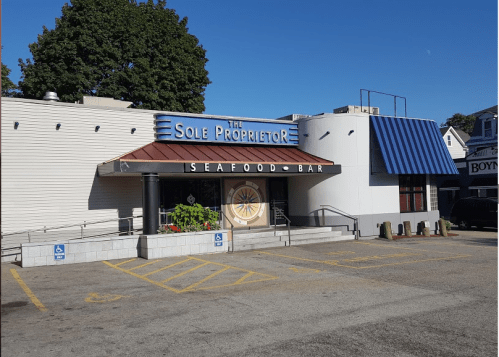 Exterior of The Sole Proprietor Seafood Bar, featuring a blue awning and accessible entrance, with clear blue skies above.