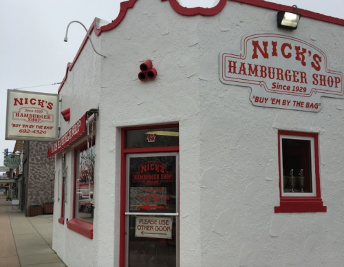 Exterior of Nick's Hamburger Shop, featuring a white building with red signage and a "Please Use Other Door" notice.