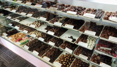 A display case filled with various types of chocolates and confections in neatly arranged trays.