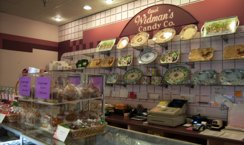 A candy shop display featuring decorative plates, candy jars, and a cash register on a pink wall.
