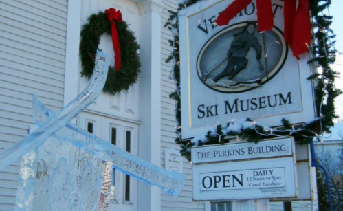 Sign for the Vermont Ski Museum with an ice sculpture and holiday decorations, featuring a wreath and red ribbons.