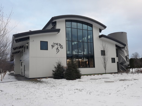 Modern building with large windows, featuring a logo, surrounded by snow and bare trees.