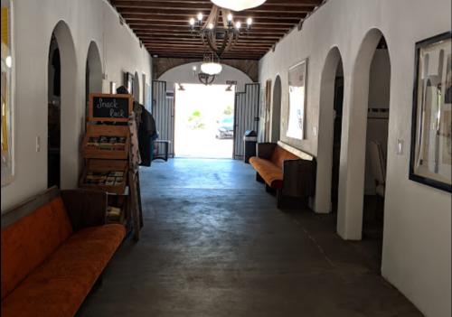 A hallway with arched doorways, orange benches, a snack rack, and light fixtures, leading to an outdoor view.