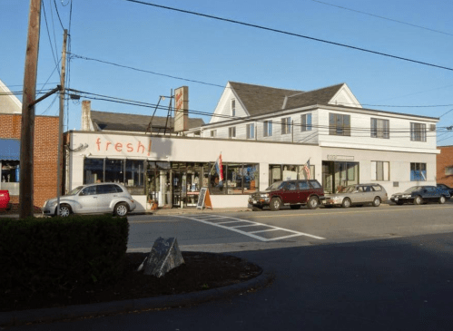 A storefront labeled "fresh" with a modern design, surrounded by parked cars and power lines on a clear day.